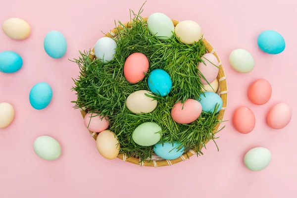 Vue du dessus des œufs de Pâques dans une assiette en osier avec herbe isolée sur rose — Photo de stock