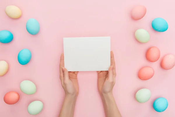 Partial view of girl holding blank greeting card isolated on pink with easter eggs — Stock Photo