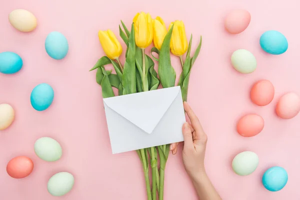 Vista parcial de la mujer sosteniendo sobre aislado en rosa con flores de tulipán y huevos de Pascua - foto de stock