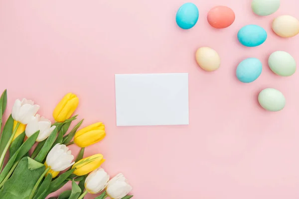 Vue du haut de la carte de vœux vide avec des fleurs de tulipes et des œufs de Pâques au pastel isolés sur rose — Photo de stock