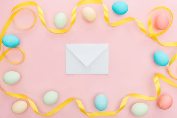 Vista superior de fita e ovos de páscoa isolados em rosa com envelope de saudação — Fotografia de Stock