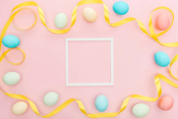 Top view of ribbon and pastel easter eggs isolated on pink with empty frame — Stock Photo