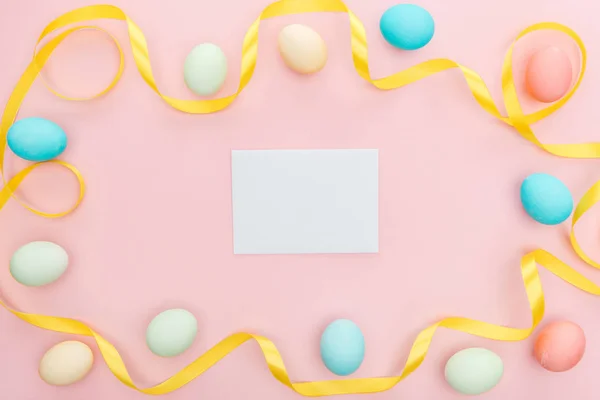 Vista dall'alto di nastro e uova di Pasqua isolate su rosa con biglietto di auguri vuoto — Foto stock