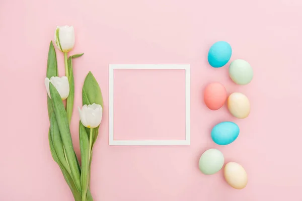 Vue de dessus des fleurs de tulipes et des œufs de Pâques avec cadre isolé sur rose — Photo de stock