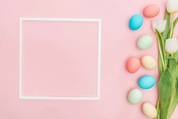 Vue de dessus des tulipes et des œufs de Pâques pastel avec cadre isolé sur rose — Photo de stock