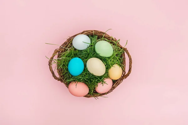 Ansicht von Ostereiern im Weidenkorb mit Gras isoliert auf rosa — Stockfoto