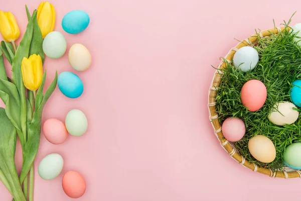 Top view of tulip flowers and pastel easter eggs in wicker plate isolated on pink — Stock Photo