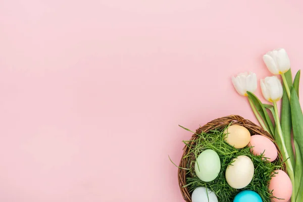 Vue de dessus des tulipes et des œufs de Pâques dans une assiette en osier isolée sur rose avec espace de copie — Photo de stock