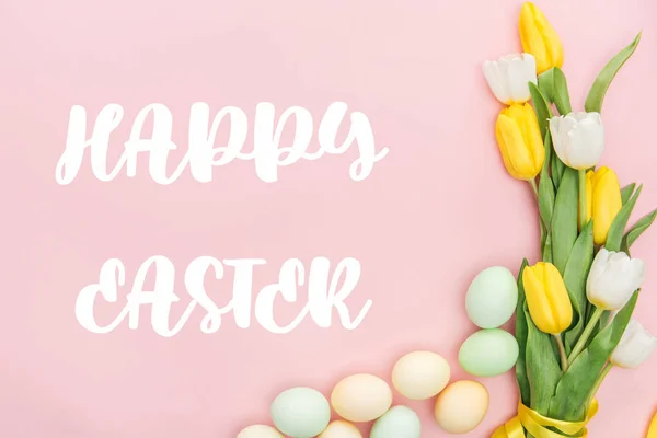 Vista superior de tulipas e ovos pintados com letras Happy Easter isolado em rosa — Fotografia de Stock