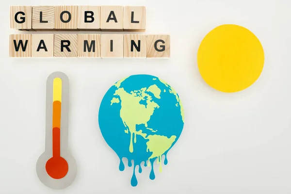 Corte de papel derritiendo tierra y sol, termómetro con indicación de alta temperatura a escala, y cubos de madera con letras de 