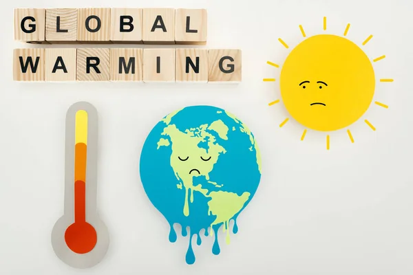 Paper cuts melting earth and sun with sad face expressions, thermometer, and wooden cubes with 