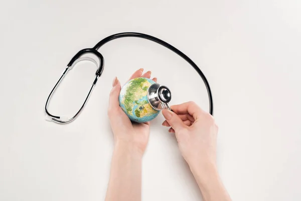 Vue partielle de la femme tenant le stéthoscope et le modèle de la terre sur fond blanc, concept de réchauffement climatique — Photo de stock