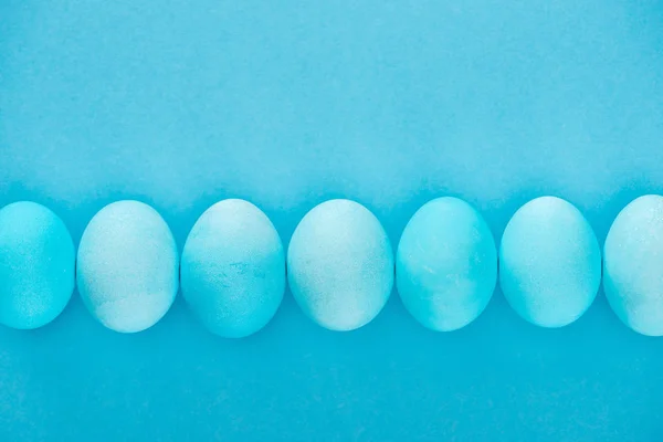 Верхний вид голубых пасхальных яиц в ряд изолированы на синий — стоковое фото
