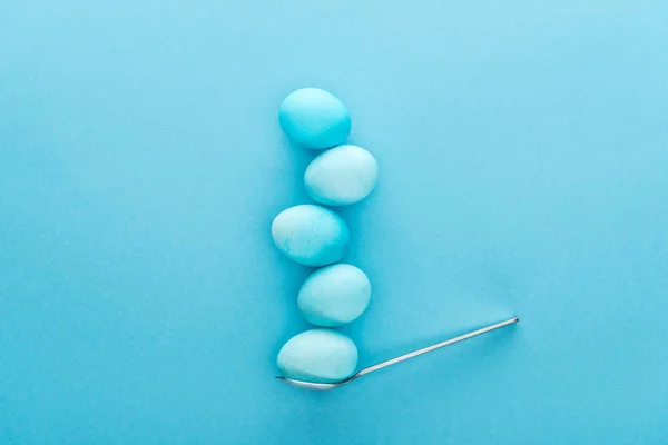 Верхний вид окрашенных пасхальных яиц на ложке изолированы на синий — стоковое фото