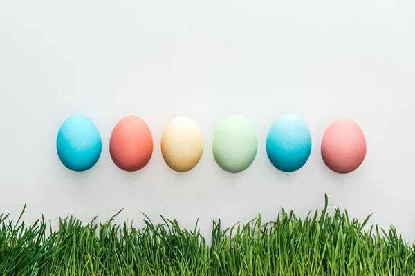 Vue de dessus des œufs de Pâques colorés isolés sur gris avec de l'herbe — Photo de stock