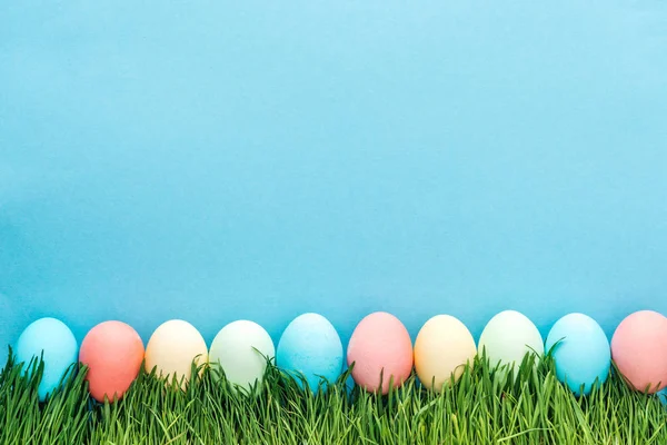 Top view of colorful easter eggs on grass isolated on blue — Stock Photo
