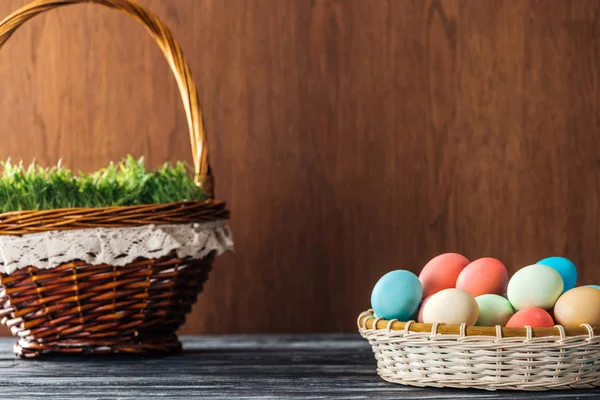 Cesta de vime com grama e tigela com ovos de Páscoa em fundo de madeira — Fotografia de Stock