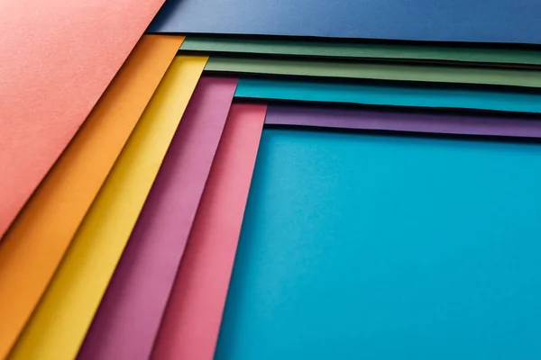 Blank blue, burgundy, orange, green, yellow, pink and purple sheets of paper on blue background — Stock Photo