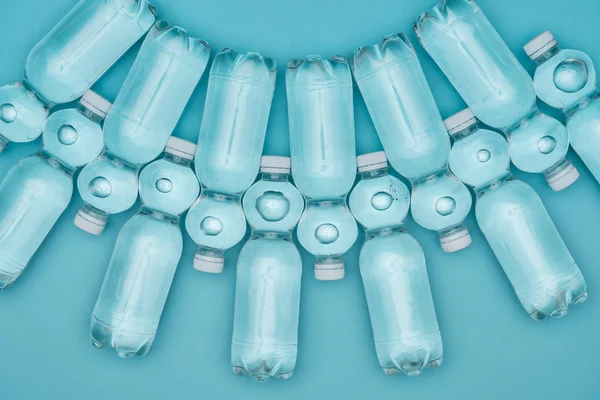 Vue de dessus des bouteilles d'eau en plastique transparent disposées en rangées isolées sur turquoise — Photo de stock