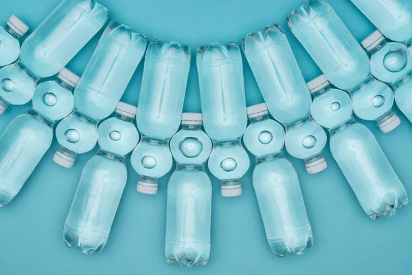 Ansicht von transparenten Wasserflaschen aus Kunststoff, die reihenweise isoliert auf Türkis angeordnet sind — Stockfoto