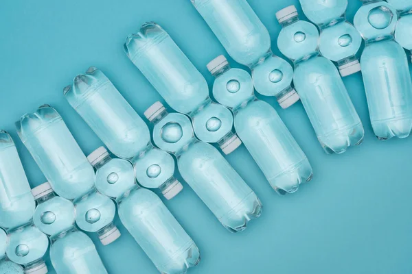 Вид пластиковых бутылок с водой, расположенных рядами, изолированных на бирюзовой — стоковое фото