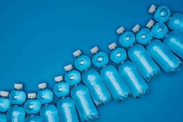 Top view of plastic water bottles in row isolated on blue with copy space — Stock Photo