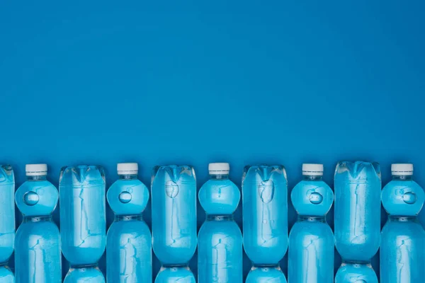 Vista superior de garrafas de água de plástico dispostas isoladas em azul com espaço de cópia — Fotografia de Stock