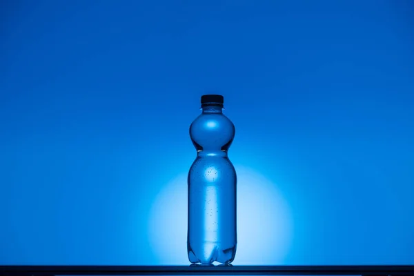 Imagem tonificada de garrafa de água de plástico no fundo azul néon com espaço de cópia e retroiluminado — Fotografia de Stock