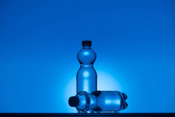 Imagen tonificada de botellas de agua de plástico sobre fondo azul neón con espacio de copia y retroiluminación - foto de stock