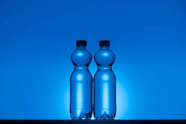 Imagen tonificada de botellas de agua de plástico transparente sobre fondo azul neón con espacio de copia y retroiluminación - foto de stock