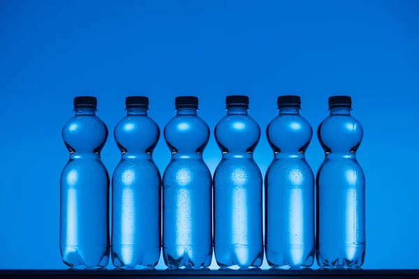 Imagen tonificada de botellas de agua de plástico sobre fondo azul neón con luz de fondo - foto de stock