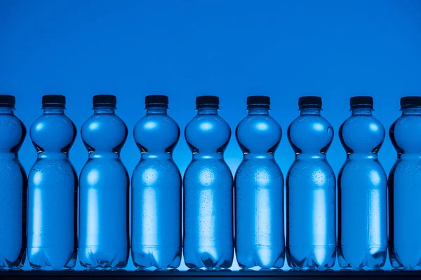 Immagine tonica di bottiglie d'acqua di plastica su sfondo blu neon con retroilluminazione — Foto stock