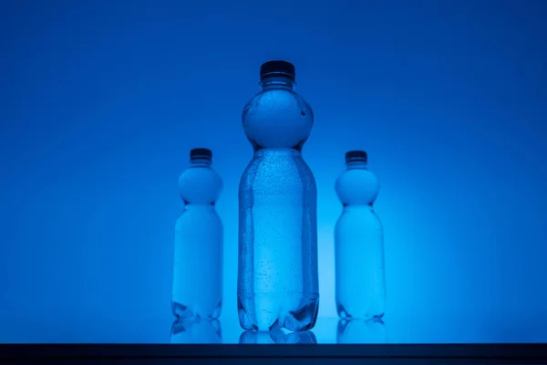 Imagen tonificada de botellas de agua de plástico sobre fondo azul neón con retroiluminación y espacio de copia — Stock Photo