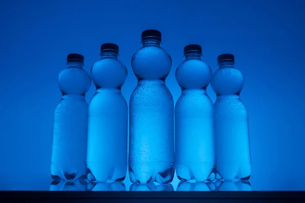 Bouteilles d'eau transparentes en rangée sur fond bleu néon — Photo de stock