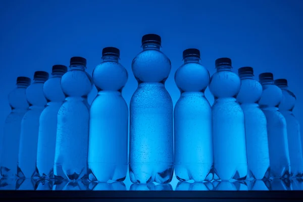 Тонированное изображение пластиковых бутылок с водой в ряд на неоновом синем фоне — стоковое фото