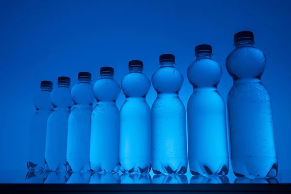 Прозорі пляшки води на неоновому синьому фоні — стокове фото