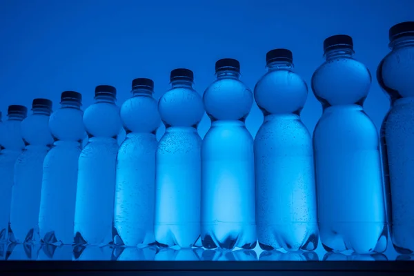 Transparent water bottles in row on neon blue background — Stock Photo