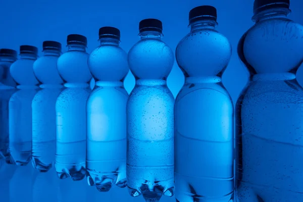 Arranjado garrafas de água transparentes em linha no fundo azul néon — Fotografia de Stock