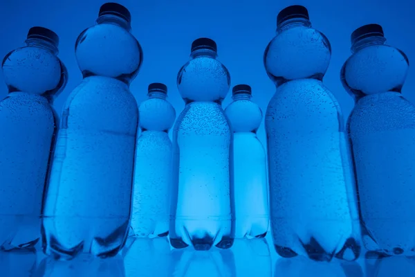 Getöntes Bild von Plastikwasserflaschen in Reihen auf neonblauem Hintergrund — Stockfoto