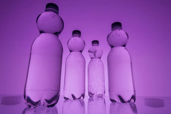 Тоноване зображення пластикових пляшок води на неоновому фіолетовому фоні — стокове фото