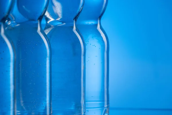 Primer plano de botellas de agua de plástico con burbujas en fila sobre fondo azul con espacio de copia — Stock Photo