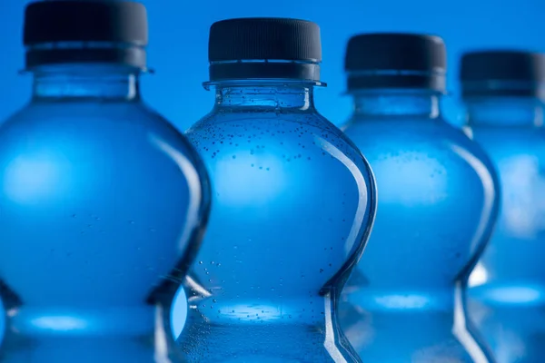 Primer plano de botellas de agua de plástico transparente con burbujas en fila sobre fondo azul - foto de stock