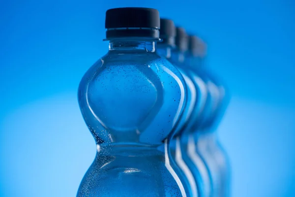 Primer plano de botellas de agua de plástico transparente con burbujas en fila sobre fondo azul - foto de stock