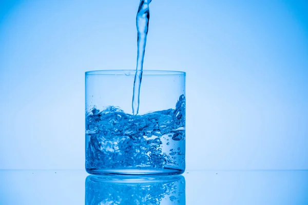 Toned image of water pouring in glass on blue background with copy space — Stock Photo