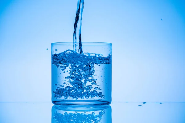 Immagine tonica di acqua versando in vetro su sfondo blu — Foto stock