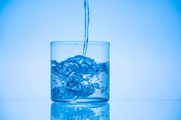 Imagen tonificada de agua vertiendo en vaso de beber sobre fondo azul con espacio de copia - foto de stock