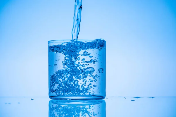 Toned image of water pouring in full glass on blue background — Stock Photo
