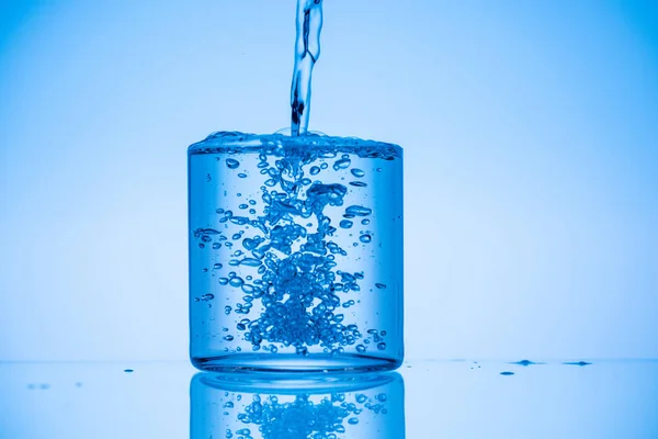 Immagine tonica di acqua versando in pieno vetro su sfondo blu — Foto stock