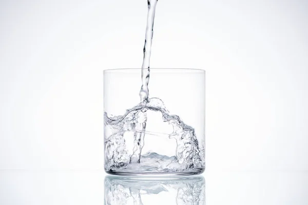 Water pouring in glass on white background with backlit and copy space — Stock Photo