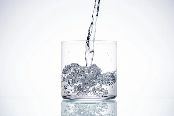 Наливая воду в стекло на белом фоне с подсветкой и копировальным пространством — Stock Photo